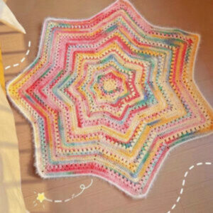 A handmade crochet blanket in the shape of a star, featuring textured stitches and a soft, neutral color palette.
