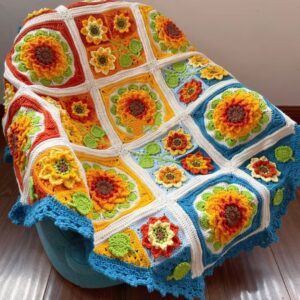 Handmade crochet sunflower blanket, showcasing vibrant yellow sunflowers on a soft, textured cream background. A cozy and cheerful home decor piece