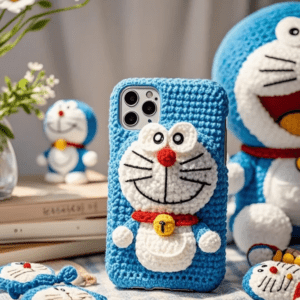 A blue and white handmade crochet Doraemon-themed phone case with embroidered facial features and signature bell detail.