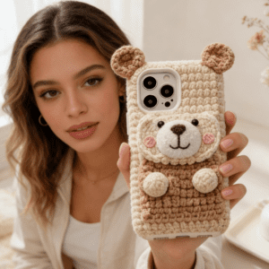 A close-up of a handmade crochet cute bear phone case with textured yarn and embroidered facial details.