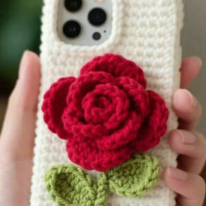 A handmade crochet rose phone case featuring a three-dimensional pink rose with green leaves attached to a soft plush case, displayed on a light background.