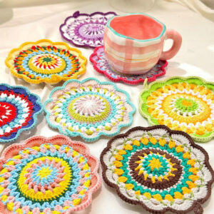 A vibrant handmade crochet mandala coaster in rainbow colors with intricate circular patterns, displayed on a light wooden surface.